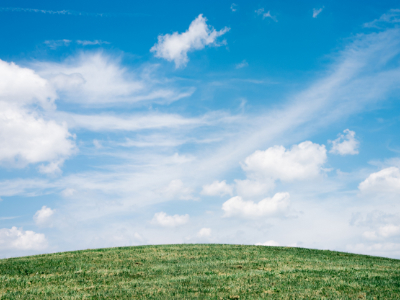 Pod modrým nebem s mráčky ležící zelená louka